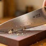 Gros plan réaliste d’un couteau de cuisine japonais affûté avec précaution sur une pierre à aiguiser humide.